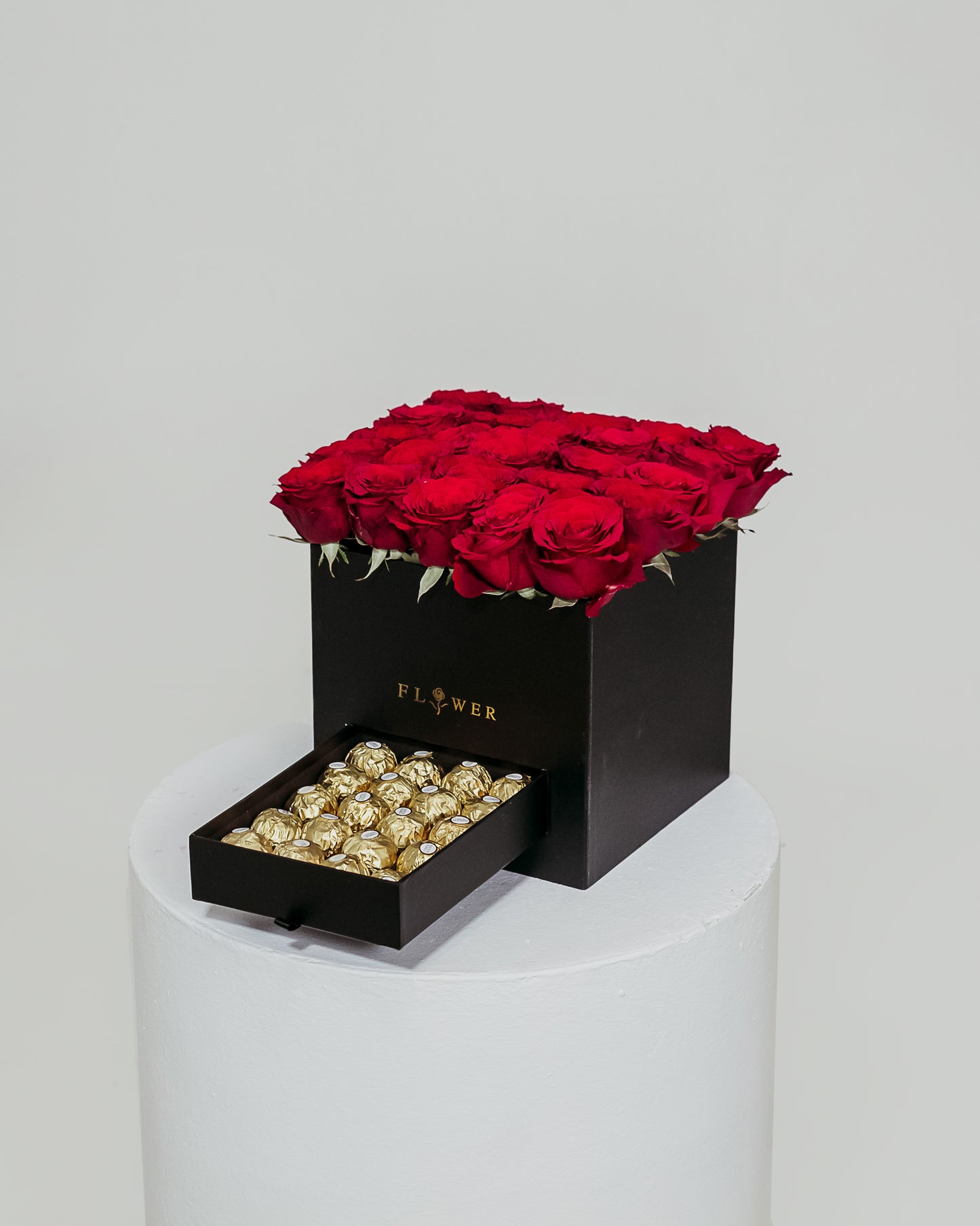 A black box filled with vibrant red roses, accompanied by a drawer containing indulgent Ferrero Rocher chocolates, an exquisite Valentine's Day gift.
