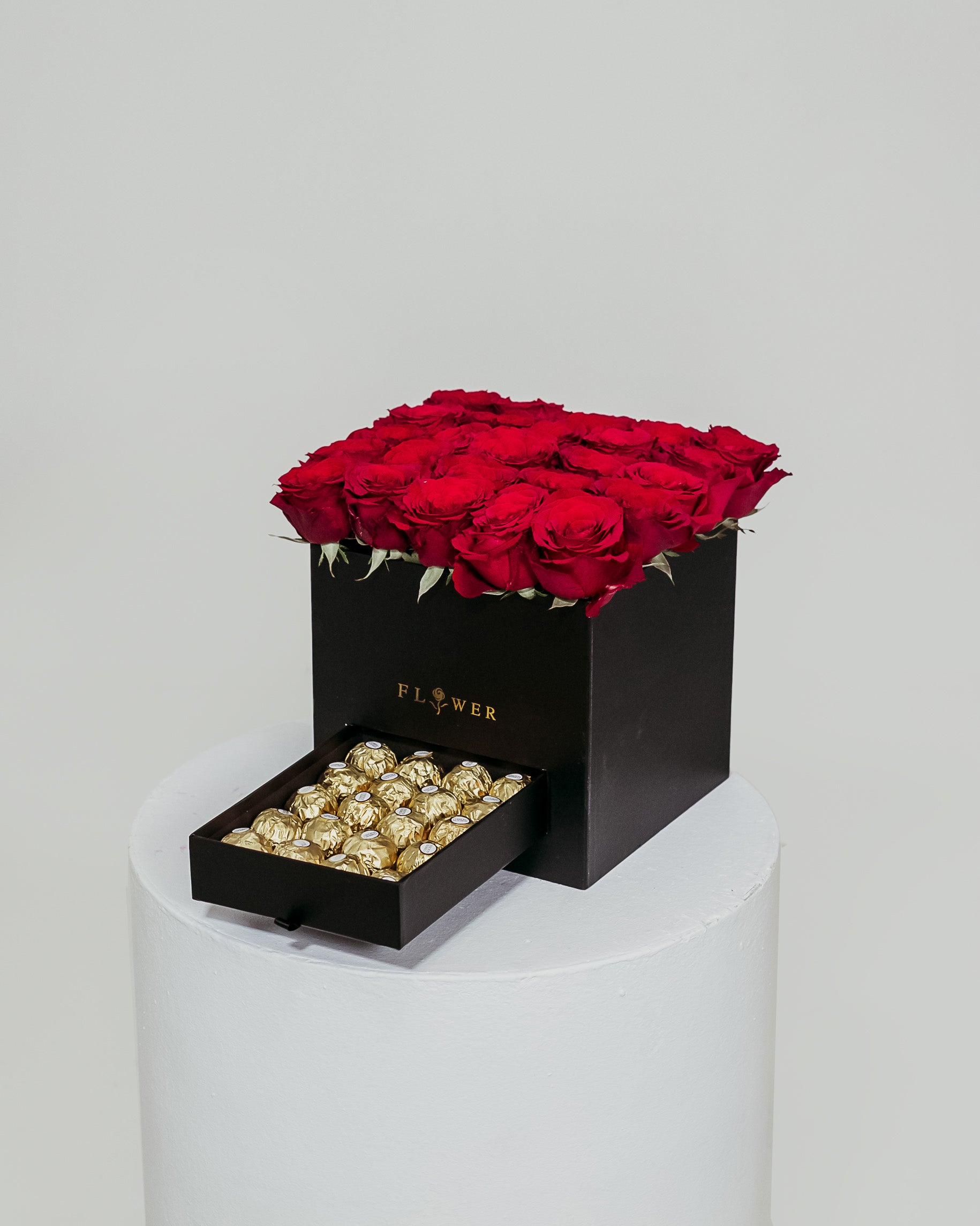 A black box filled with vibrant red roses, accompanied by a drawer containing indulgent Ferrero Rocher chocolates, an exquisite Valentine's Day gift.