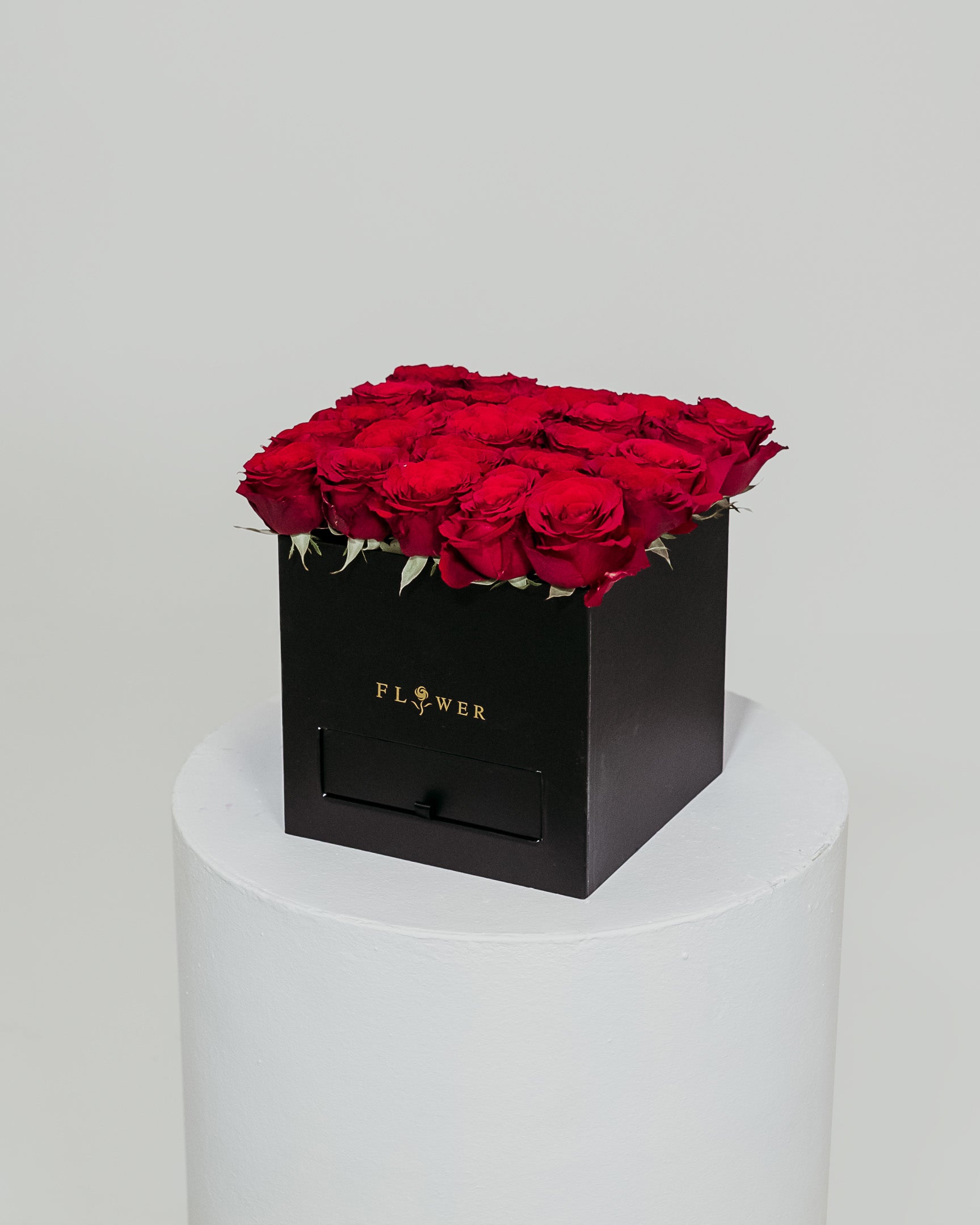 A sophisticated black box filled with vibrant red roses, accompanied by a drawer containing Ferrero Rocher chocolates