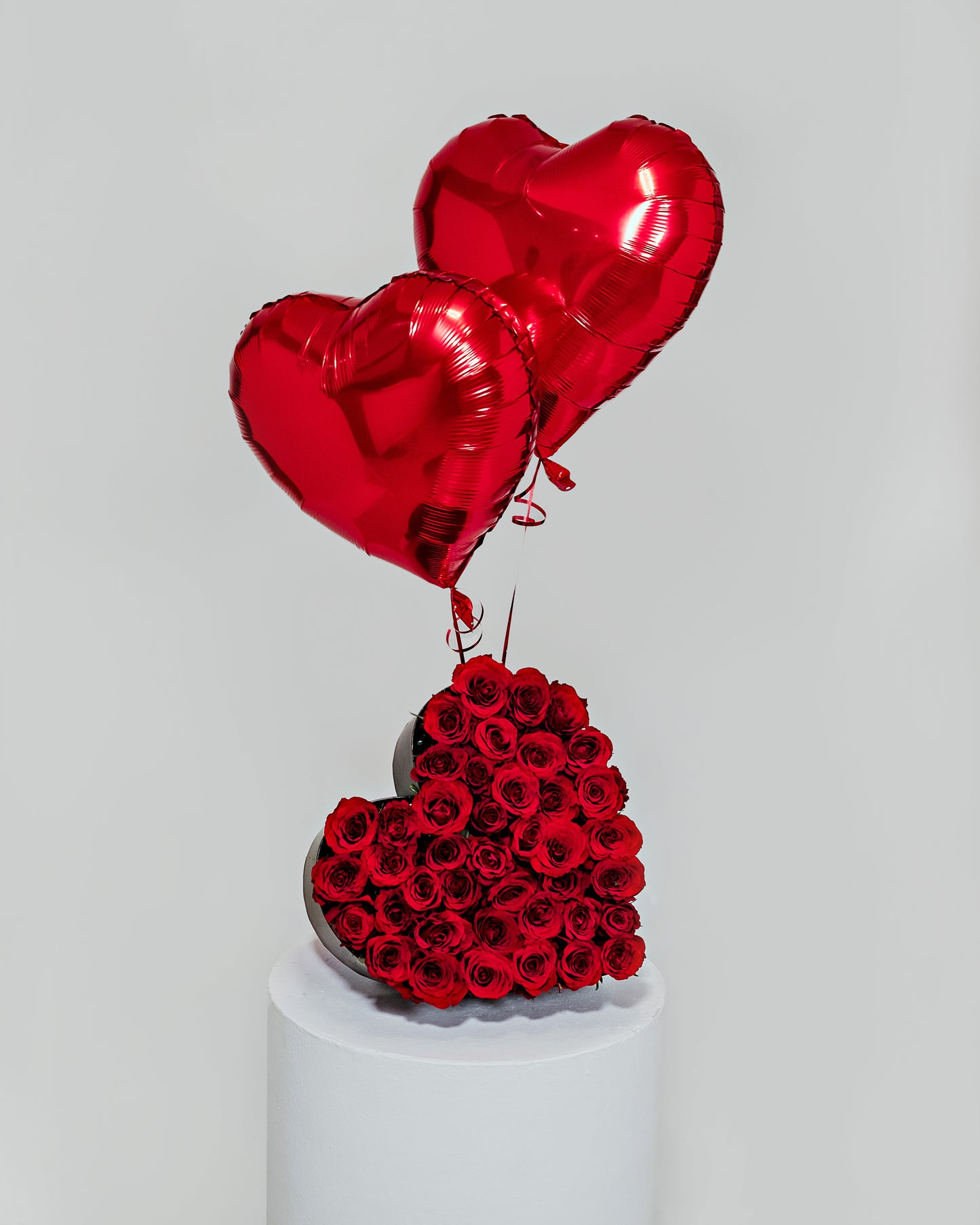 A large, striking heart-shaped arrangement formed with lush red roses and accented with heart-shaped balloons, a grand declaration of love for Valentine's Day.