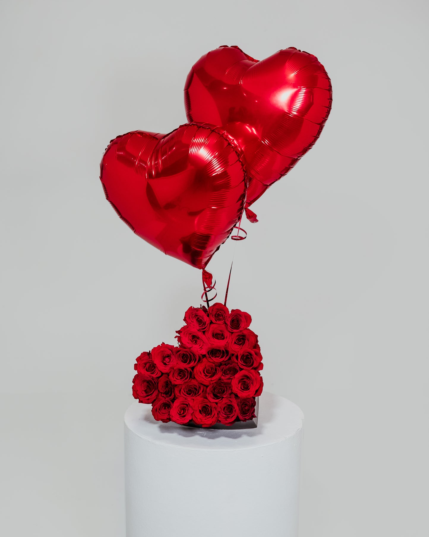 A medium-sized heart-shaped arrangement crafted from vibrant red roses, adorned with heart-shaped balloons, a delightful expression of love for Valentine's Day.